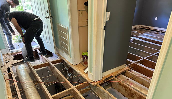 Workers removing a damaged floor and subfloor, exposing the joists below