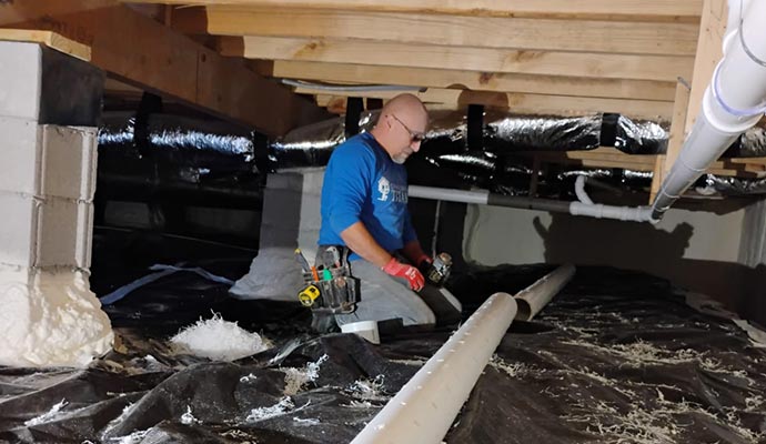 A worker installing a PVC drainage pipe system in a crawlspace