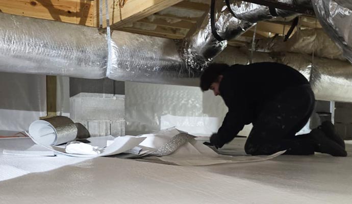 A worker installing a white vapor barrier during a crawlspace encapsulation