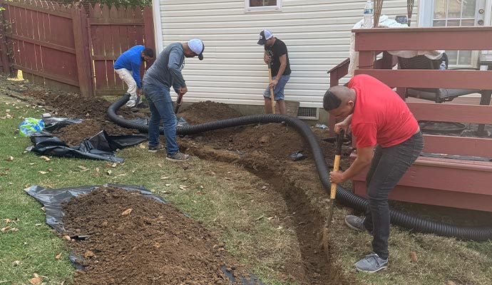 A team of workers digging a trench and installing a French drain in a backyard