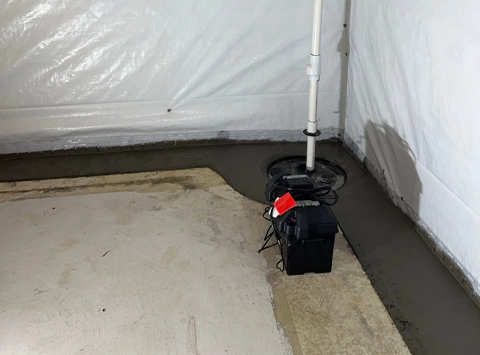 A newly waterproofed basement floor with a perimeter drain and a black submersible sump pump installed, ready to prevent water intrusion.