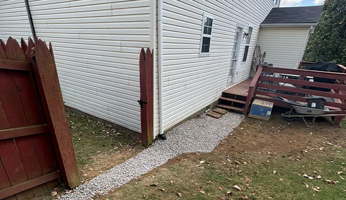 A newly installed exterior French drain with gravel along a house foundation