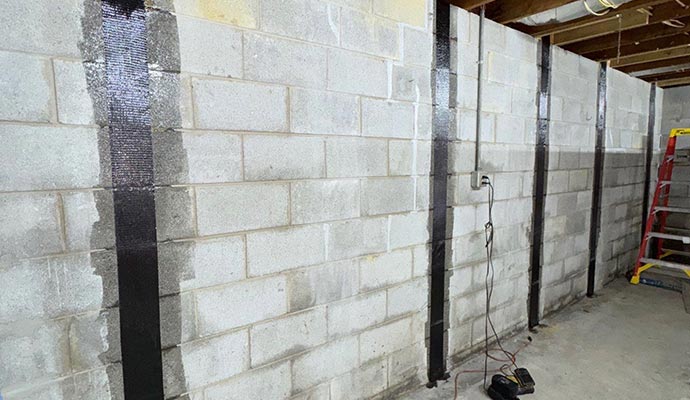 A concrete block basement wall reinforced with vertical carbon fiber straps to stabilize structural bowing and cracks