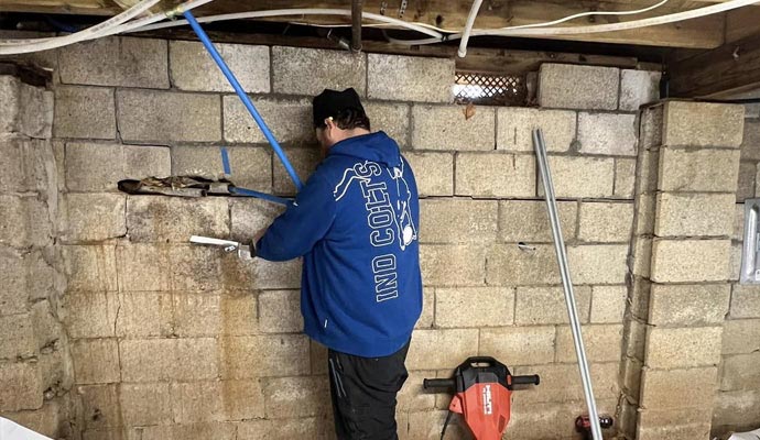 A technician working on a concrete block foundation wall with visible horizontal cracks