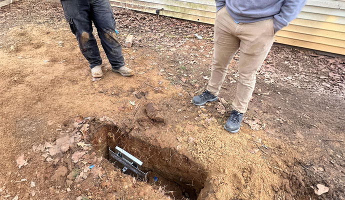 Excavated hole with metal foundation bracket embedded in soil near building exterior