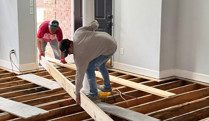 Two workers installing wood flooring over exposed joists