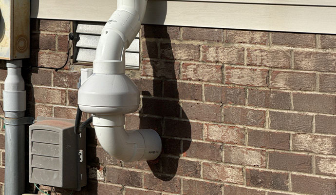 Installed radon mitigation system with vent pipe and fan unit on exterior brick wall